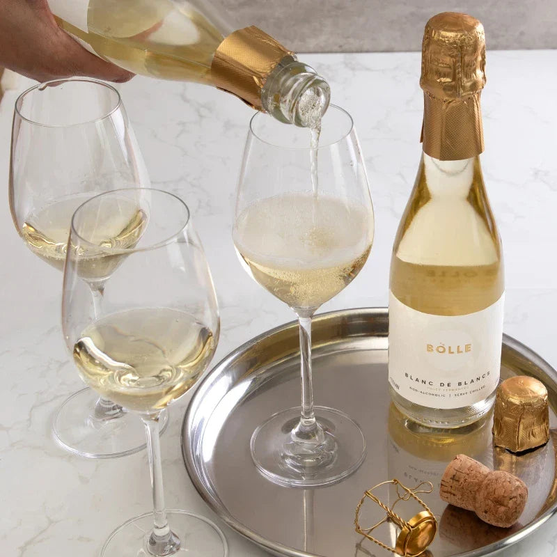 Bottle of Bolle Blanc de Blancs being poured into a glass with a tray of wine glasses and bottles on a marble surface.