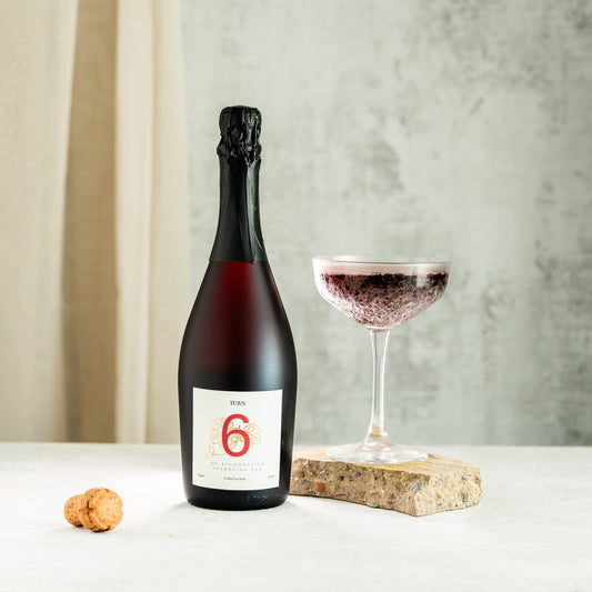 Bottle of red wine with a glass on a white surface