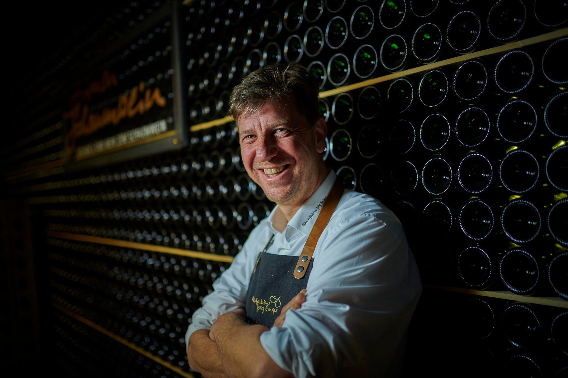 Man standing in front of a wine cellar with bottles on shelves.