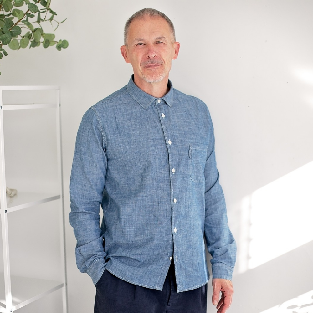 Man wearing a blue shirt standing indoors with a white background