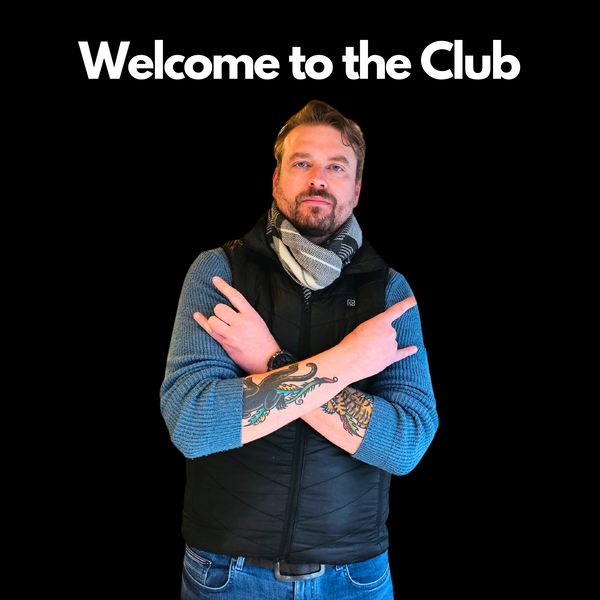Man with tattoos wearing a blue sweater and black vest with 'Welcome to the Club' text.