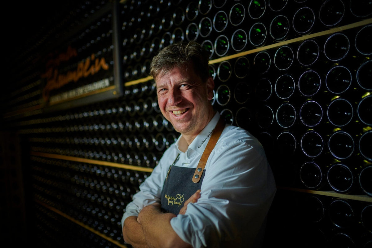 Man standing in front of a wine cellar with bottles on shelves.