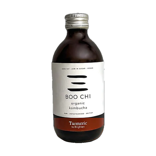 A dark glass bottle of Boo Chi Turmeric organic kombucha with a white label, a rust red band and a silver cap.