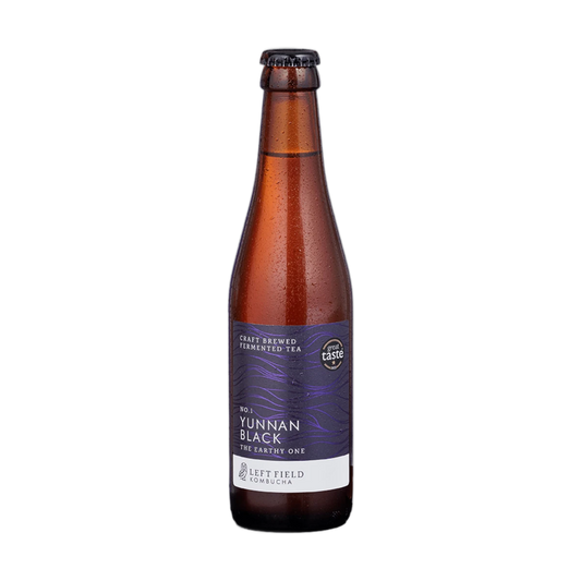 Left Field No.1 Yunnan Black raw kombucha in a tall amber 330ml glass bottle with a black cap and a deep purple wave-patterned label.
