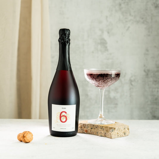 Bottle of red wine with a glass on a white surface