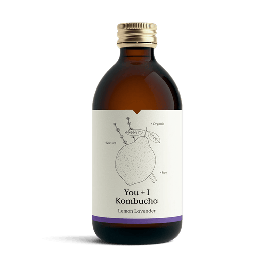 You + I Lemon & Lavender raw kombucha in an amber glass bottle with a gold cap and a cream label with a botanical line drawing and a purple band.